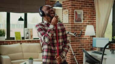 Afro-Amerikalı bir insan ahşap yerleri silmek, evi temizlemek ve kulaklıkla müzik dinlemek için paspas kullanıyor. Gülümseyen genç adam temizlik ve ev işlerini zevkle yapıyor..