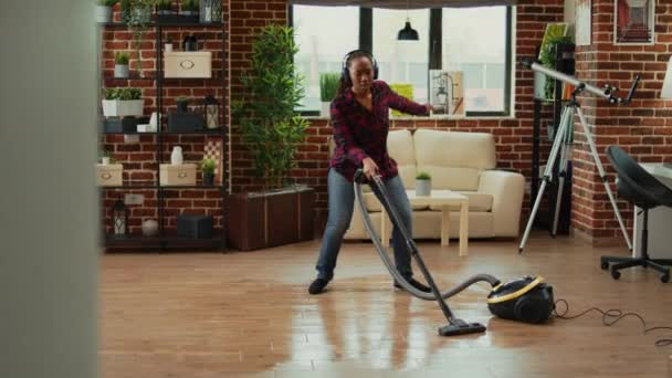 African American Housewife Using Vacuum Cleaner Listening Music Headset Enjoying — Vídeos de Stock