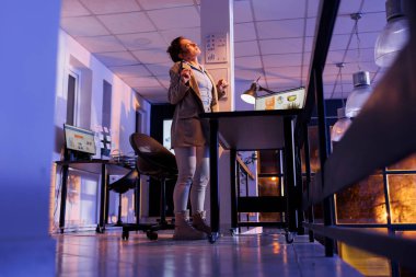 Tired manager stretching body for relaxing while working overtime at investment strategy, planning to increase company profit. Entrepreneur analyzing marketing graph report in startup office