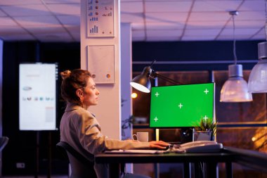 Entrepreneur analyzing green screen mock up chroma key computer with isolated screen, analyzing marketing report. Businesswoman working overtime at company strategy in startup office
