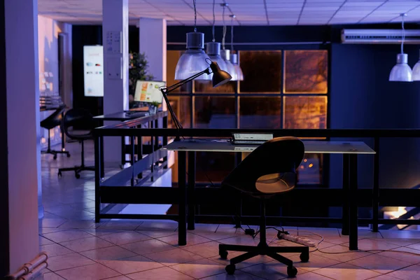 Interior of empty business office with modern furniture during night time, having financial graphics report running on the computer screen. Marketing company with nobody in it, place of work startup
