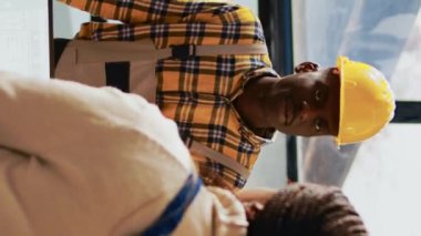 Dikey video: Mutlu çalışanlar depoda eğleniyor, imalat malzemeleri ve stok dağıtımı üzerinde çalışıyor. Ürünlerle gülen ve plan yapan insanlardan oluşan bir ekip. El kamerasıyla..