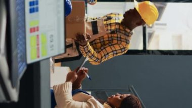 Dikey video: Afro-Amerikan işçiler depoda stok dağılımı planlıyorlar, paketlerdeki mallarla çalışıyorlar. Bir grup insan depo ürünlerini raflarda depolamak için kullanıyor.