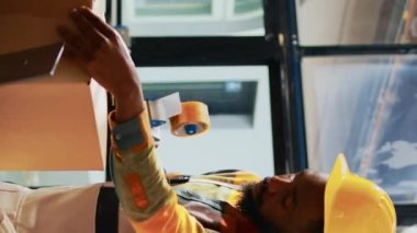Dikey video: Depo çalışanlarının malzeme dolu kutuları ambalajlamaları, lojistik planlamak için dizüstü bilgisayarları kullanmaları. Erkekler ve kadınlar, konteynır ve karton paketlerde, raflarda nakliye için mallarla çalışıyorlar.
