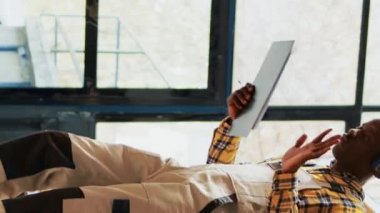 Dikey video: Depoda dans hareketleri gösteren erkek işçi, perakende ürün konteynerleriyle depoda çalışıyor. Depoda şarkı söyleyerek, dans ederek, imalat sektöründe eğlenen genç adam.