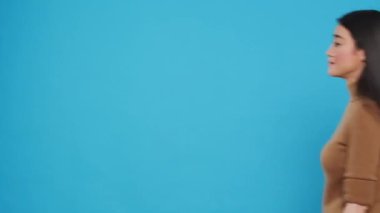 Smiling cleaning lady wearing yellow rubber gloves standing with arm crossed in studio over blue background. Cheerful asian housekepper took great care in customer housecleaning duties
