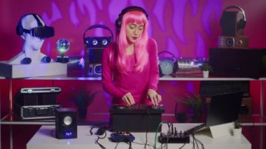 Musician with pink hair performing techno music using dj mixer console enjoying to play song with fans, having fun during night party. Artist doing performance with professional audio equipment