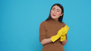Smiling asian maid clapping hands in front of camera after finishing to do house cleaning, standing in studio over blue background. Housekepper took great pride in her housekeeping duties