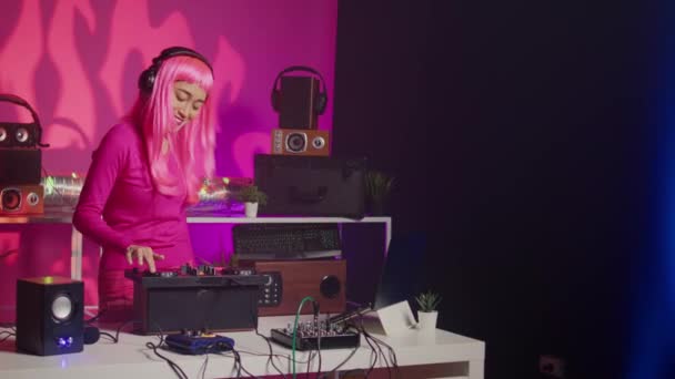 ミキサーで電子歌を演奏するヘッドフォンを持つアジアのミュージシャン クラブで夜にファンと楽しいDjテーブルに立って ピンクを背景にスタジオでテクノ音楽を演奏するアーティスト — ストック動画