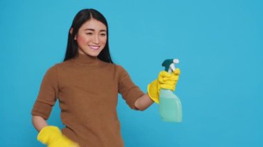Cheerful housekepper using sponge and professional cleaning detergent while cleaning client home, using cleanliness equipment. Cleaner wore gloves as part of her attire while doing the housework.
