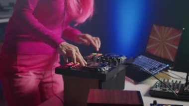 Musician mixing electronic sound with techno, enjoying party with fans, standing at dj table performing concert in club at night. Asian artist with pink hair performing music using turntables