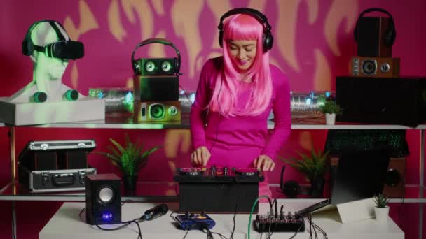 Djの女性は ナイトクラブでテクノパーティー中にオーディオ機器を使用して音楽を混合し始める前にヘッドフォンを置く ピンクの髪を持つアジアのパフォーマーミキサーコンソールで音楽パフォーマンスを作成します — ストック動画