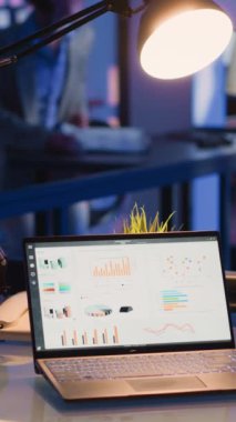 Vertical video: Startup worker typing financial data report on screen, looking at business diagrams and graphs for corporate investment. Young employee working overtime in office, planning progress.