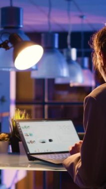 Vertical video: Business manager checking research project overtime working late on computer to plan financial report. Young advisor sitting at desk analyzing online statistcs for startup growth