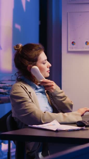 垂直ビデオ オフィスの経済統計のための机の分析図で固定電話の呼び出しに答えるビジネス女性 電話回線の財務分析レポートを扱う社員 — ストック動画
