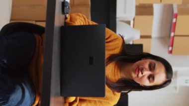 Vertical video: Asian owner doing supplies logistics with laptop, writing inventory information on files for startup business development. Entrepreneur planning products shipment in storage room.