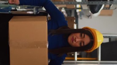 Vertical video: Asian woman in wheelchair carrying cardboard boxes to do quality control, working with employees. Female worker looking at merchandise in storage room, supply chain management.