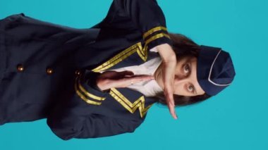 Vertical video: Professional stewardess showing t shape sign in studio, asking for pause and refusing to work. Young confident air hostess in uniform doing break and rejection gesture over blue