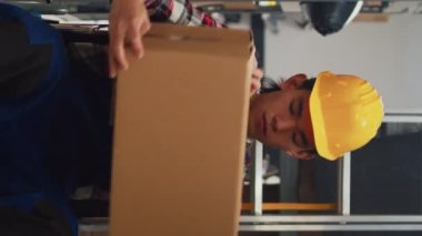 Vertical video: Man in wheelchair working in storage room with goods, employee with chronic impairment carrying boxes to check merchandise before shipment. Guy working in disability friendly space.