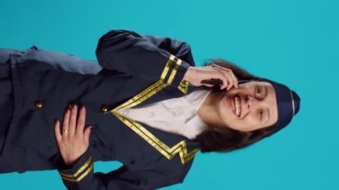Vertical video: Young airliner chatting on mobile phone call and having fun, feeling happy and having remote discussion. Cheerful air hostess wearing aviation uniform for flying industry, phone line.