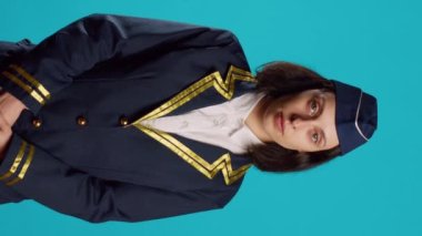 Vertical video: Smiling young woman working as air hostess, wearing flying uniform and posing with confidence. Cheerful stewardess preparing for commercial flight, working in aviation industry.