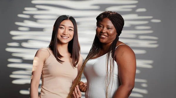 Interracial unique women creating beauty ad in studio, promoting powerful and uplifting campaign focusing on wellness and self love. Young models advertising skincare routine, promote bodycare.