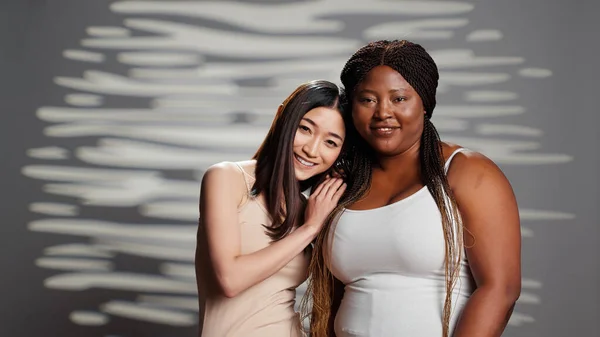 Interracial ladies being glamorous posing for skincare ad, having radiant luminous skin and promoting self acceptance. Flawless women smiling and expressing wellness and femininity.