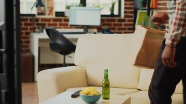 Relaxed guy having meal from fast food takeout place, unpacking food from delivery bag in front of television. Young person preparing to eat dinner and watch comedy tv show or movie on sofa.