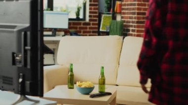African american couple unpacking delivery meal, preparing to eat fast food takeaway and drink beer at television. Young people feeling relaxed watching action movie together.