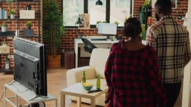 Life partners preparing to eat food from takeout bag, receiving delivery order before binge watching tv show in living room. Young people eating fast food meal for dinner, film on television.