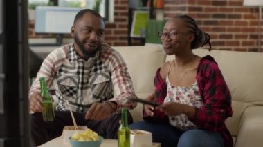 African american couple eating asian food at home, enjoying time together with takeaway meal and beer bottles. Young life partners using chopsticks to eat noodles in living room.