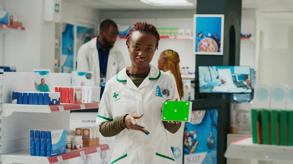 Health specialist pointing at medicine box with greenscreen, howing isolated chroma key template in pharmacy shop. Young employee holding blank copyspace background in drugstore.