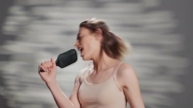 Beautiful cheerful woman singing using hair brush on camera, fooring around and acting silly. Beauty model with glowing look playing with brush to promote self love and confidence.