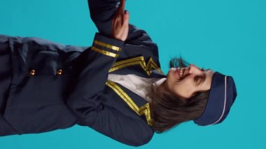 Vertical video: Professional air hostess presenting miniature toy plane, feeling happy about flying occupation. Young woman working as stewardess in uniform showing small artificial airplane on camera