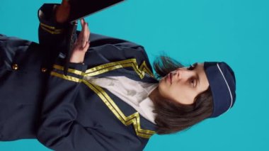 Vertical video: Young female airliner using laptop in studio, browsing online internet page and social media app. Air hostess working in aviation flying industry and holding portable pc, scrolling