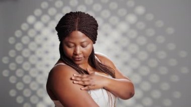 African american girl feeling radiant applying cream in studio, promoting skincare products for cosmetics campaign. Flawless woman using moisturizer or serum on camera, self love.