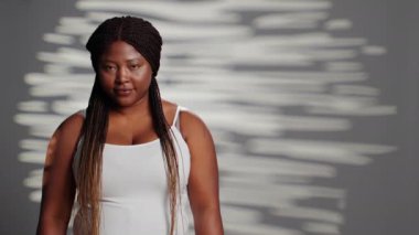 Female model embracing imperfections in studio, posing for empowering wellness ad campaign. Sensual gentle woman with luminous glowing skin feeling confident with body and skintone.