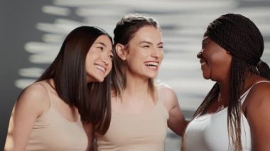 Multiethnic group of models posing for body positivity ad in studio, having fun with friends advertising skincare products. Cheerful women laughing on camera, different skintones and body types.