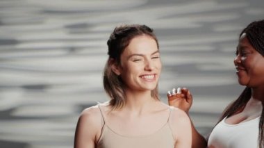 Group of confident girls promoting body acceptance on camera, laughing together and having fun with skincare body positivity campaign. Female models with different skintones and shapes.