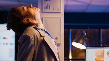 Stressed manager getting up and streching back, working late at night in business office. Young entrepreneur feeling tired and in pain, analyzing financial report for marketing.