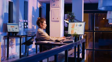 Female employee dealing with back pain at desk job, feeling sick while working on financial graphs report. Woman stretching neck and body after sitting in office. Handheld shot.