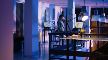 Young business woman working late in startup office, checking new financial report project for management growth. Advsor agent analyzing graphs on laptop and computer. Handheld shot.