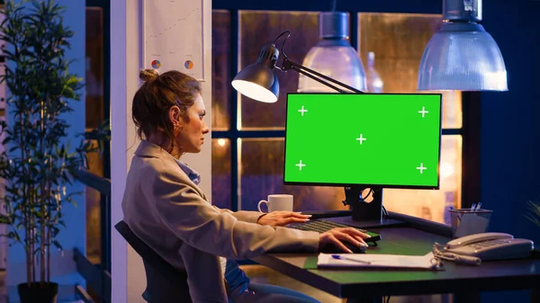 Female advisor working at night with green screen on computer, analyzing isolated display with chromakey. Young woman with corporate job using mockup screen copyspace template.