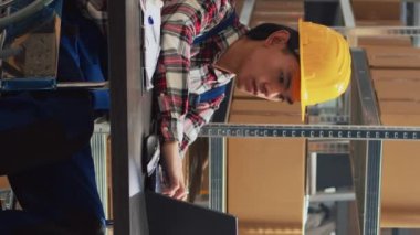 Vertical video: Young man in wheelchair looking at stock supplies, checking merchandise in boxes with female worker. Asian adult with impairment planning business development in storage room.