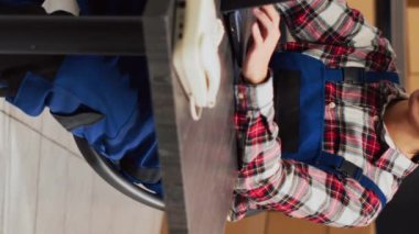 Vertical video: Asian man doing storage room inventory with laptop, organizing merchandise in boxes on shelves. Young adult working in storehouse space to plan order shipment, products distribution.