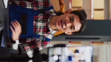 Vertical video: Male employee filming promotion video in warehouse, using social media streaming platform to promote small business in storage room. Young people doing teamwork for advertisement.