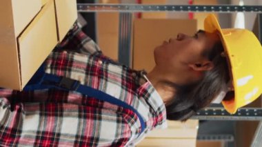 Dikey video: Asyalı adam raflardaki malzemelerle kutuları düzenliyor, depodaki kadın girişimcilerle kalite kontrol yapıyor. Çalışan paketleri rafa kaldırır, sipariş yönetimine hazırlanır.