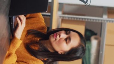 Vertical video: Female owner working in wheelchair at warehouse, using laptop to plan logistics and distribution in depot. Woman with chronic disability doing financial planning and quality control