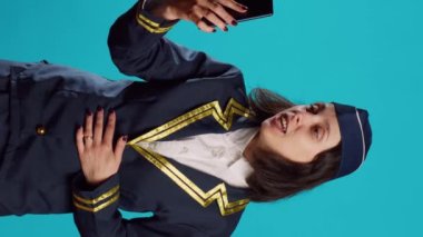 Vertical video: Air hostess attending online video call conference on smartphone, chatting on internet videoconference with webcam on camera. Young smiling stewardess talking on teleconference chat.