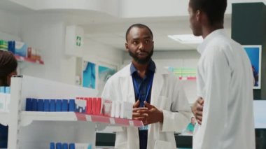 Customer asking specialist about stomachache pills, looking to buy medicaments against pain in drugstore. Young man talking to pharmacist about drugs and supplements. Handheld shot.
